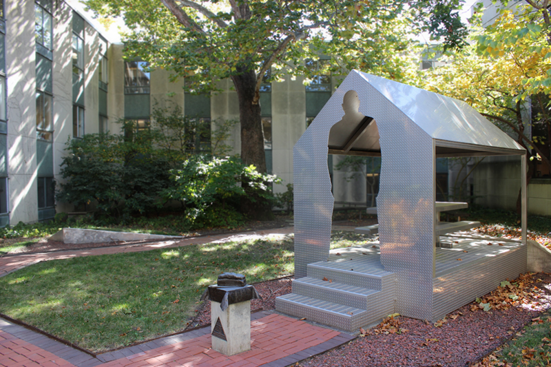 Photo of courtyard with metal sculpture of bread and metal gazebo with a person cutout for entrance and a picnic table under the gazebo