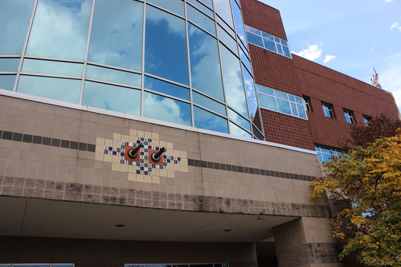 Entrance to Molecular Biology Building showing a mosaic sculpture with two black hands reaching out from the building. Black and white tiles surround the hands. The tiles have letters on them